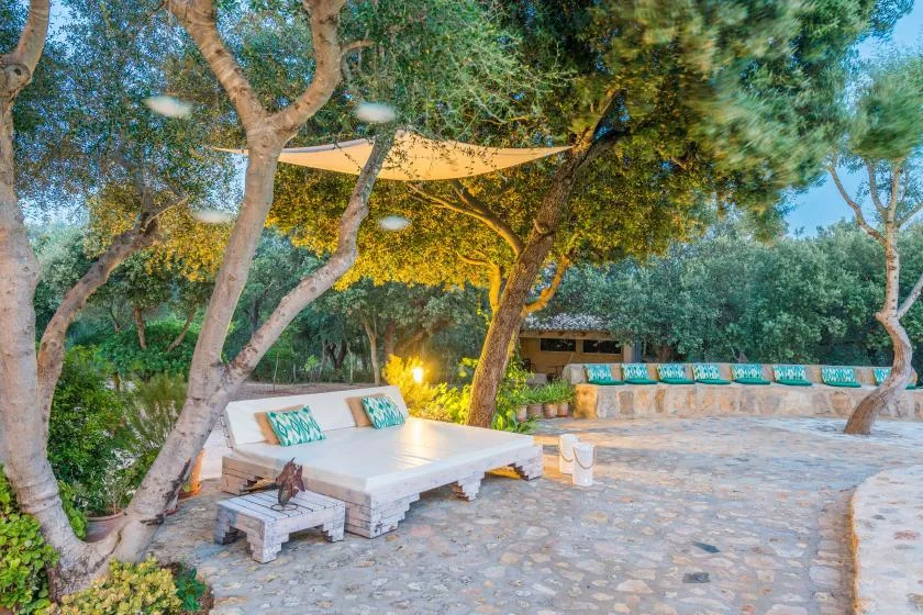 An outdoor patio with cushioned seating beneath leafy trees and a shade canopy.