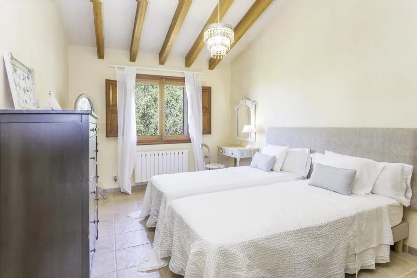 A bright bedroom with two beds, a window, and exposed ceiling beams.