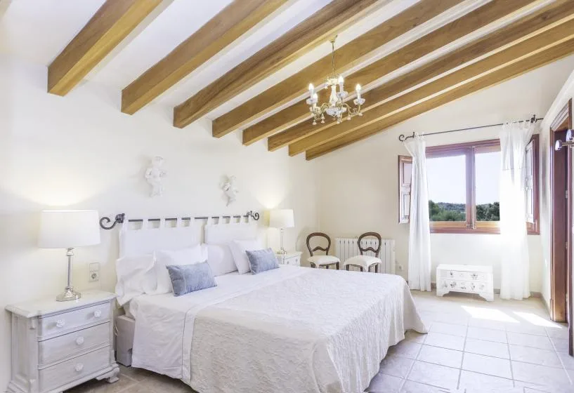 A bright bedroom with a large bed beneath exposed ceiling beams.