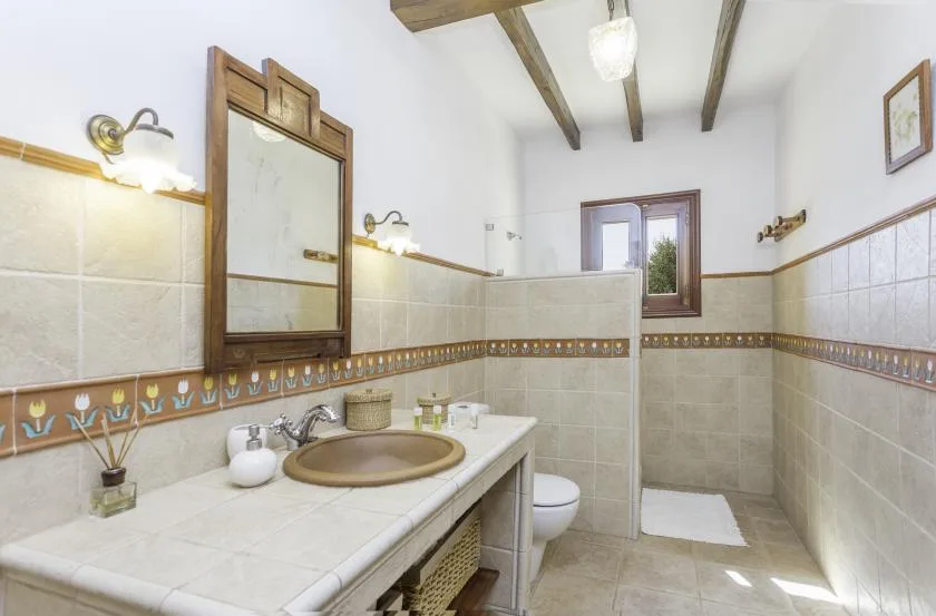 A tiled bathroom with a sink, mirror, toilet, and a window.