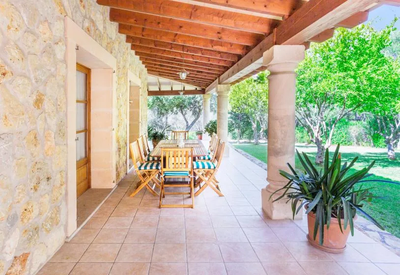 A covered patio with outdoor seating and potted greenery beside a garden.