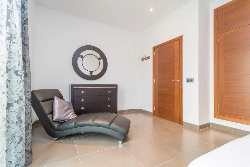 Una habitación luminosa con una butaca reclinable, una cómoda oscura y puertas de madera.