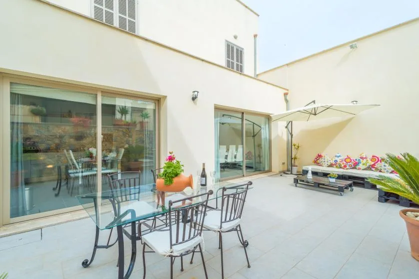 Un patio pavimentado tiene una mesa de comedor, asientos y una sombrilla grande.