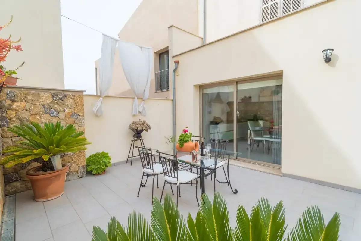 Un patio exterior pavimentado con una mesa de comedor de vidrio junto a puertas corredizas de vidrio.