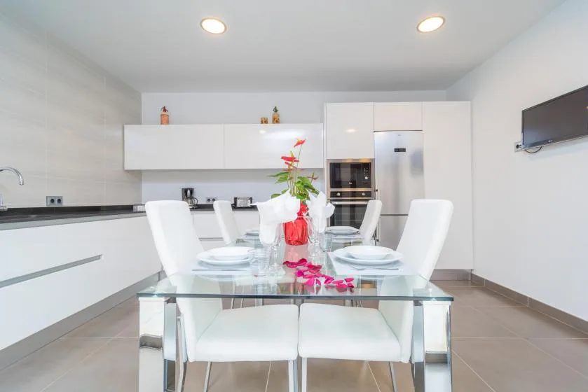 Una cocina y comedor luminosos con una mesa de vidrio y asientos blancos.