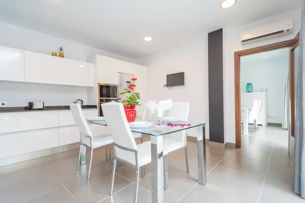 Comedor moderno con mesa de vidrio y asientos blancos junto a la cocina.