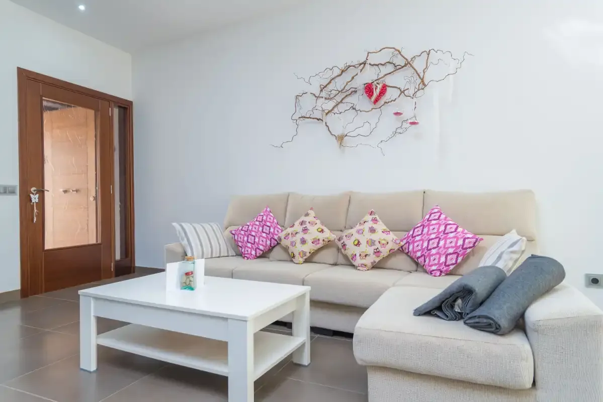 Un salón luminoso con un sofá seccional beige y una mesa de centro blanca.