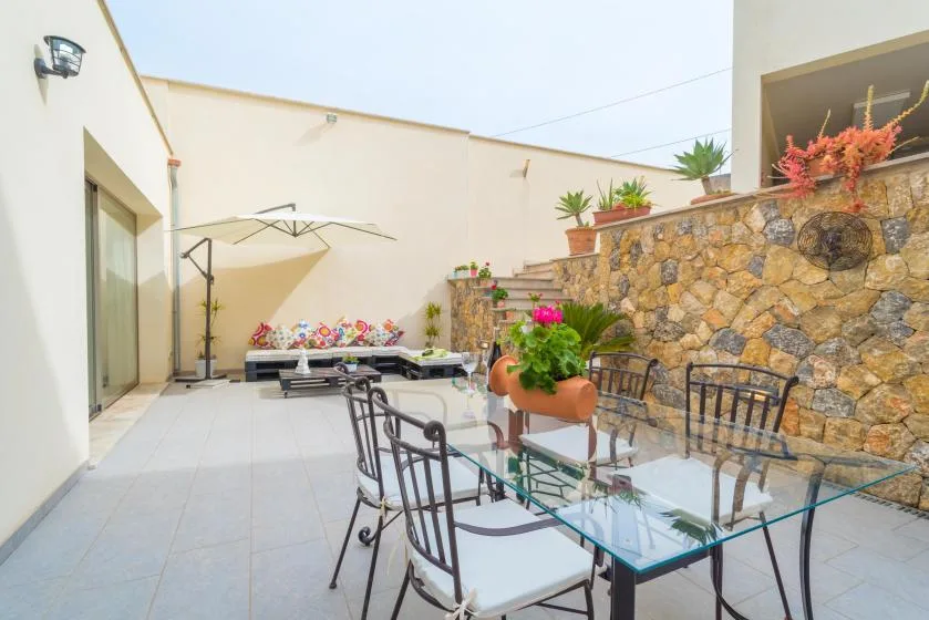 Un patio al aire libre con una mesa de comedor de vidrio y plantas en macetas junto a un muro de piedra.