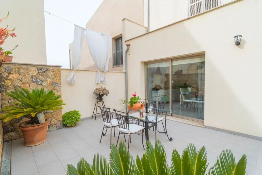 Un patio exterior embaldosado con un conjunto de comedor metálico y puertas correderas de vidrio.