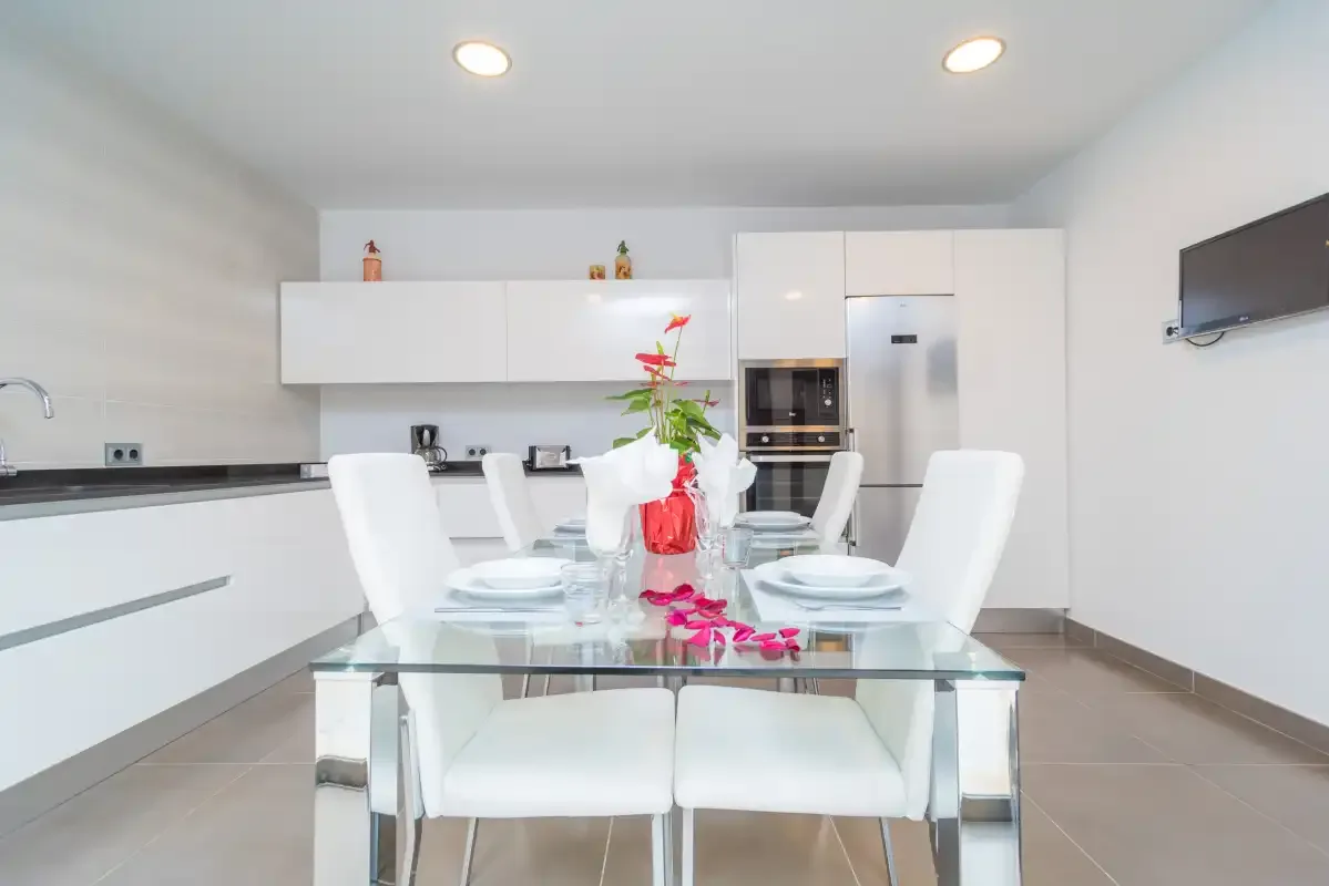 Una cocina moderna y luminosa con gabinetes blancos y una mesa de vidrio.