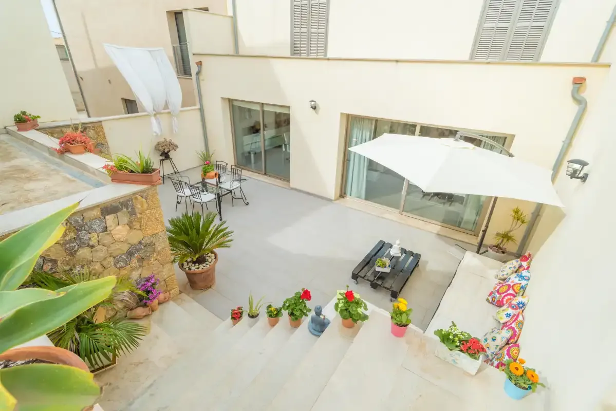 Un patio pavimentado con asientos, plantas en macetas y un toldo blanco.