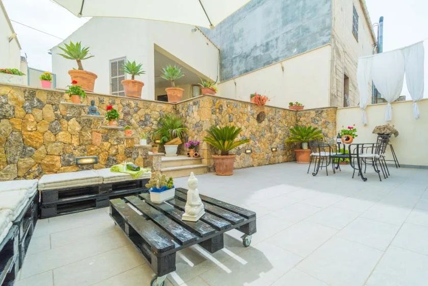 An outdoor patio with a stone wall, potted plants, and a table with chairs.