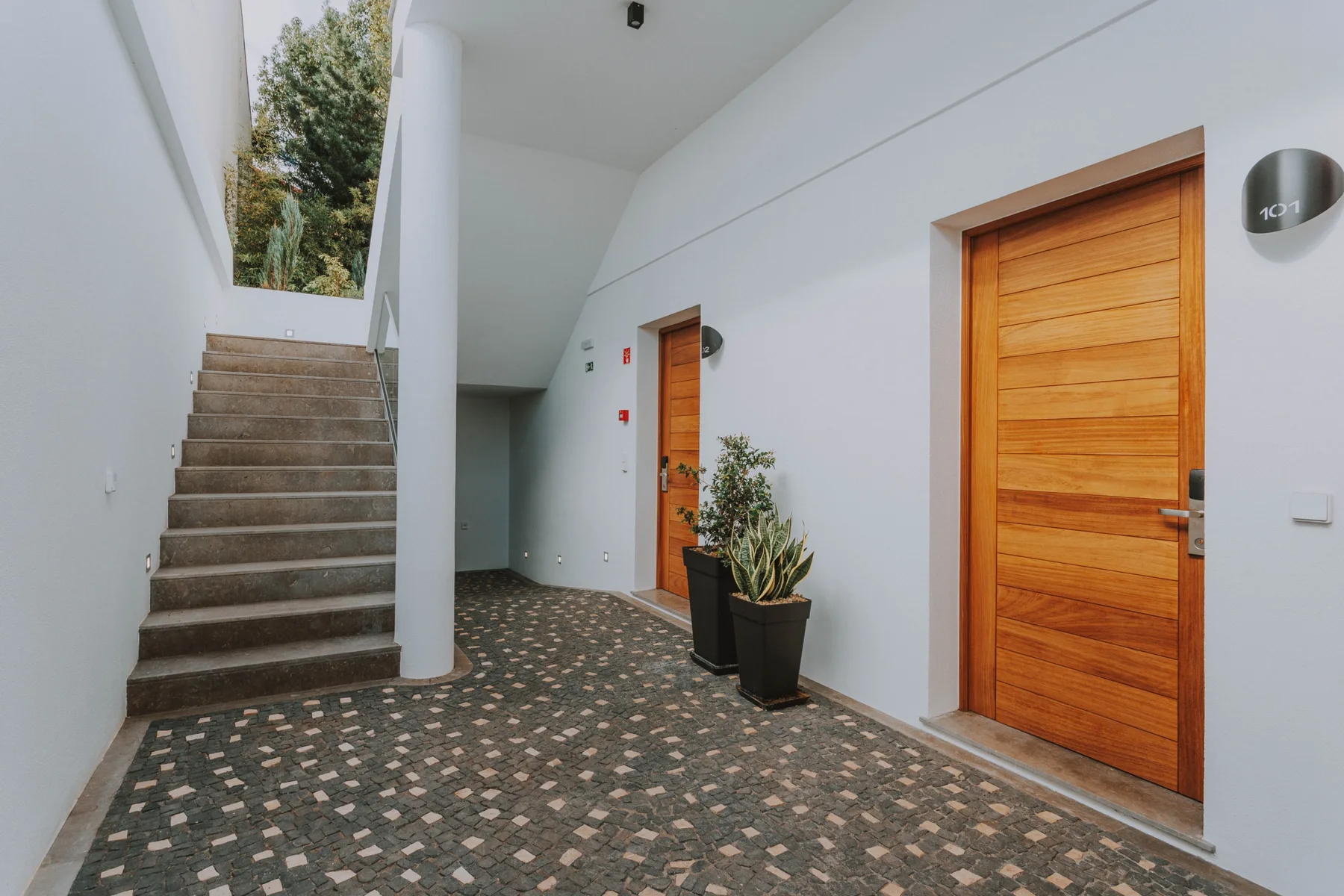 Un pasillo interior tiene suelo estampado, puertas de madera y una escalera.