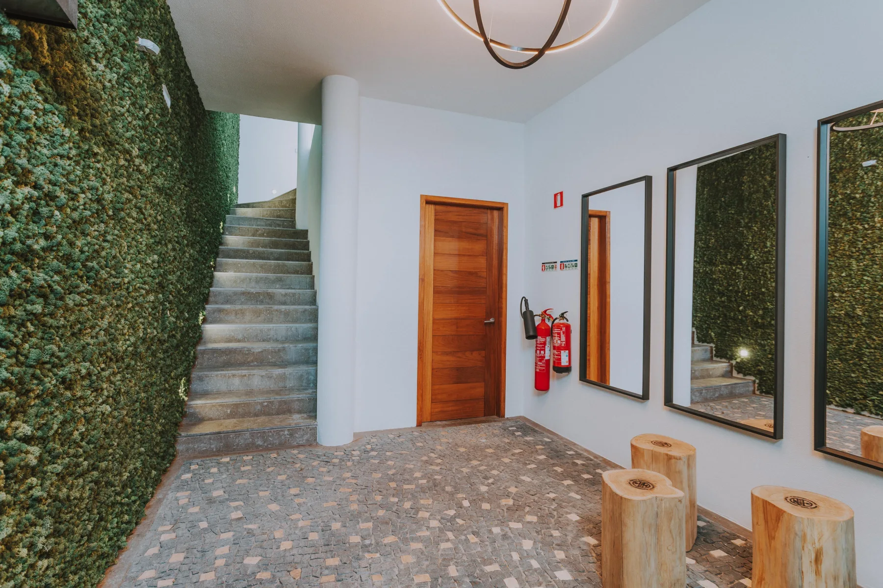 Un recibidor interior tiene una puerta de madera, una escalera y espejos en la pared.