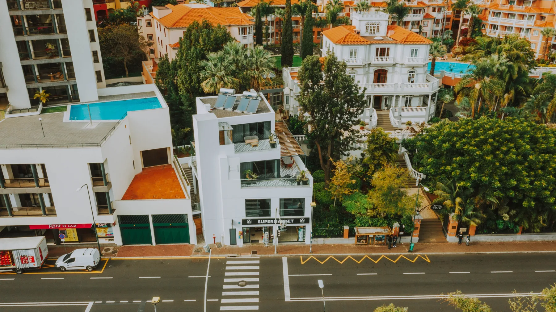 Una escena urbana con edificios modernos, vegetación y un paso peatonal señalizado.