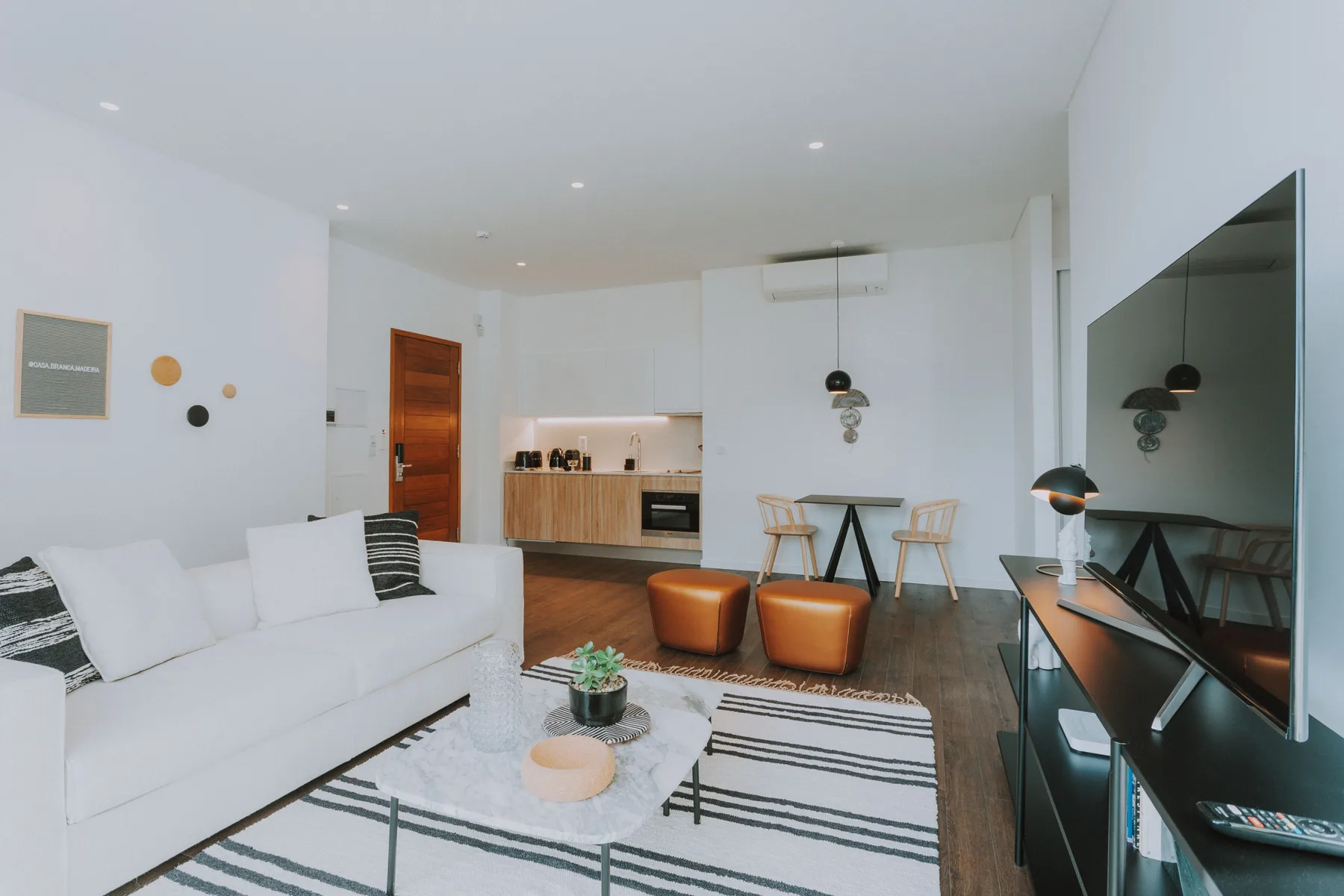 Una luminosa sala de estar con sofá blanco, alfombra a rayas y cocina abierta.