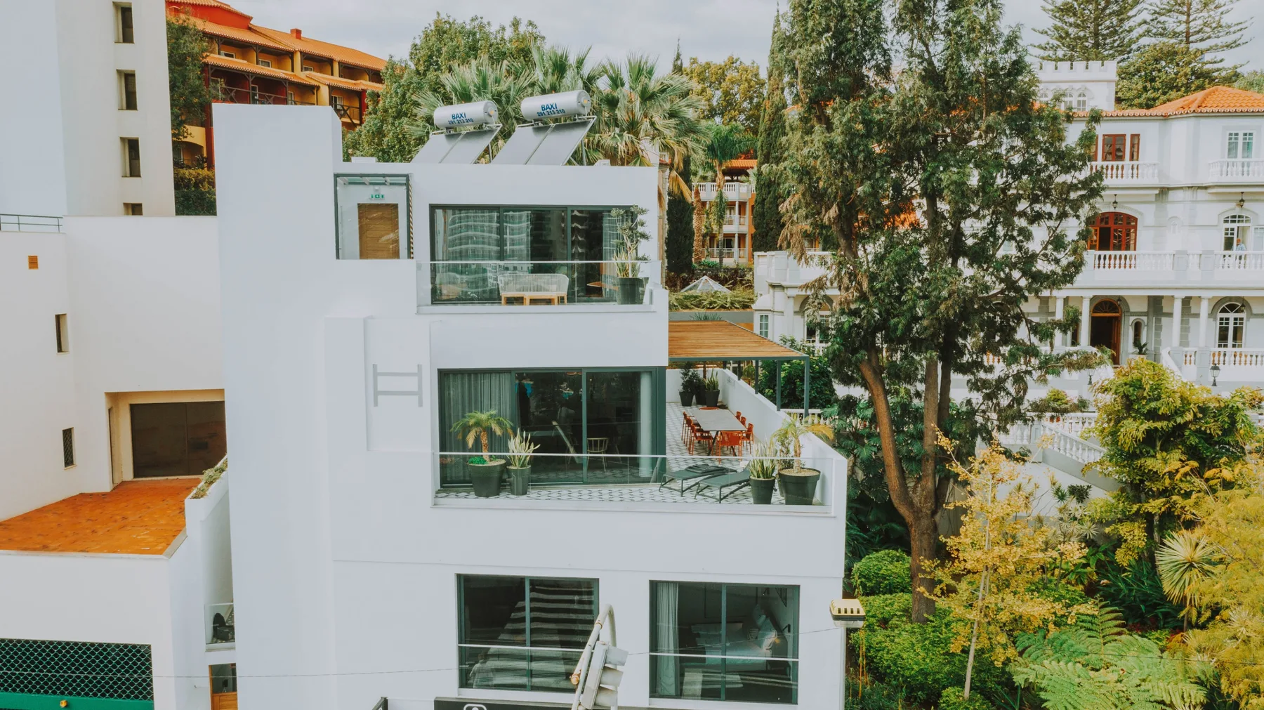 Un edificio blanco moderno con amplios ventanales se alza entre árboles y edificios vecinos.