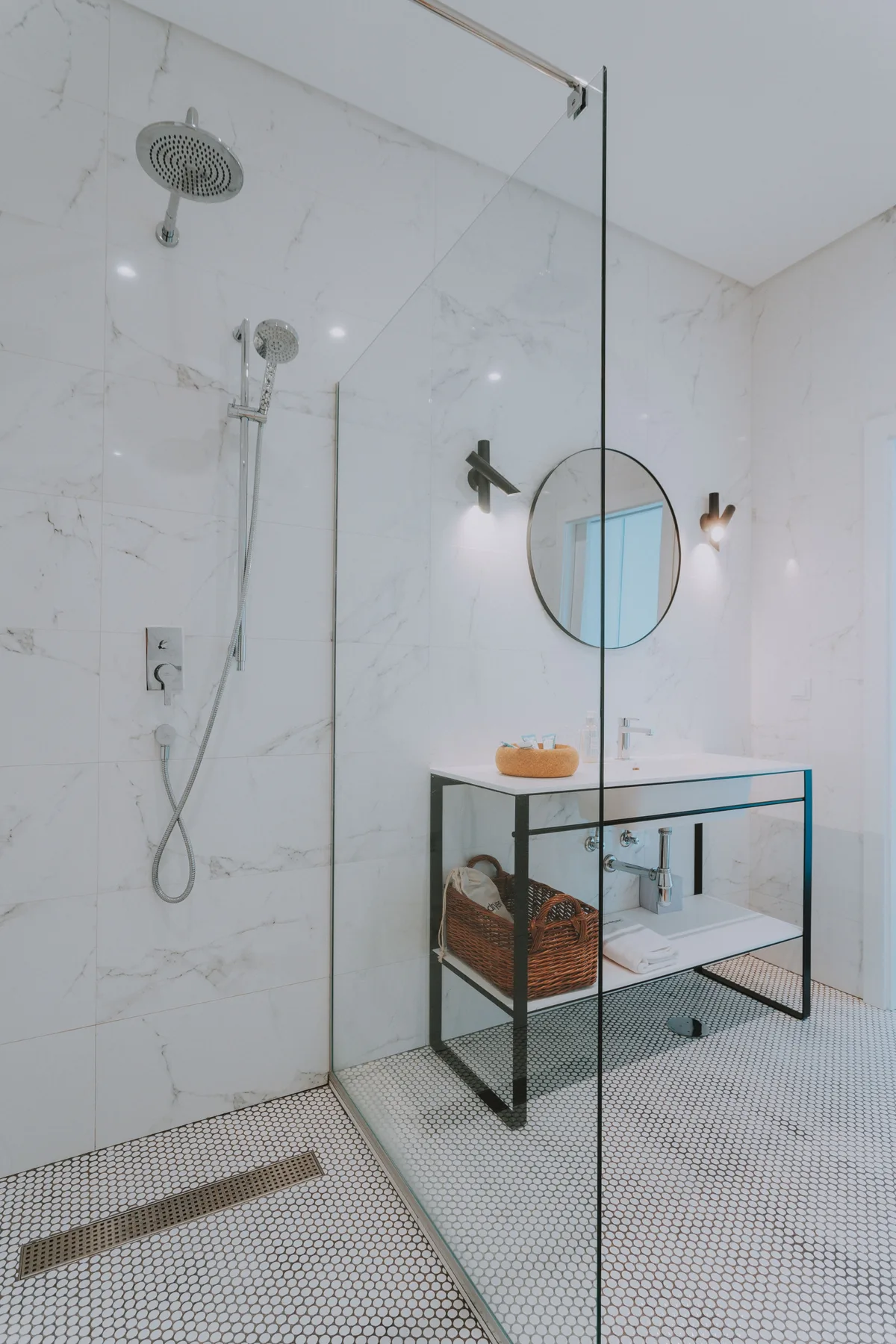 Un baño luminoso con una ducha de cristal y un lavabo bajo un espejo redondo.