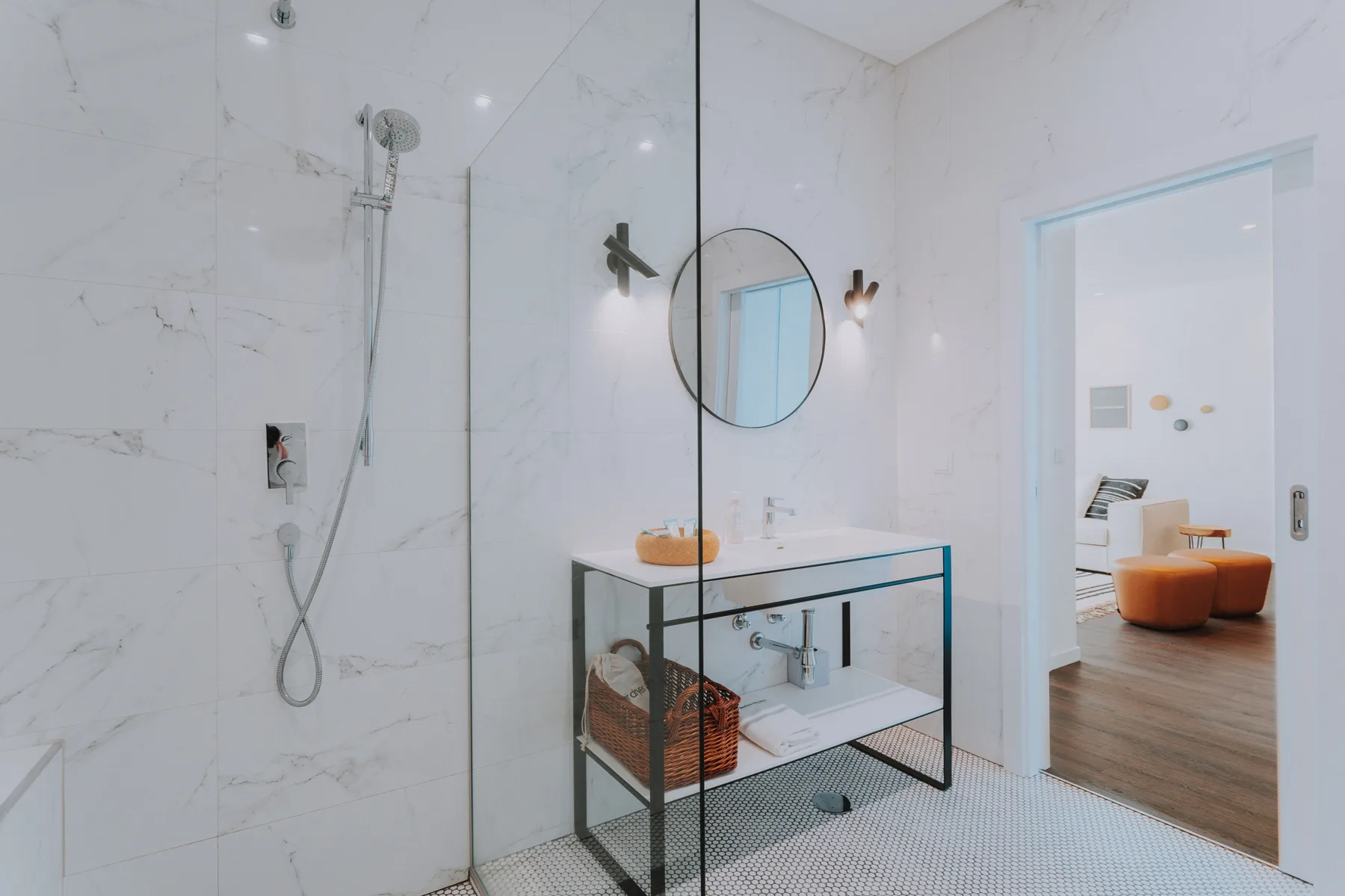 Un baño luminoso con ducha de cristal y un lavabo bajo un espejo redondo.