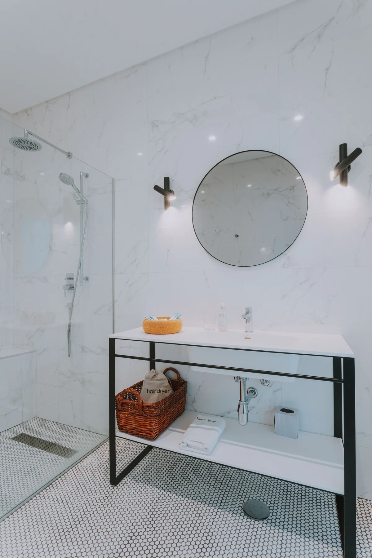 Un baño luminoso con ducha, espejo redondo y tocador abierto.