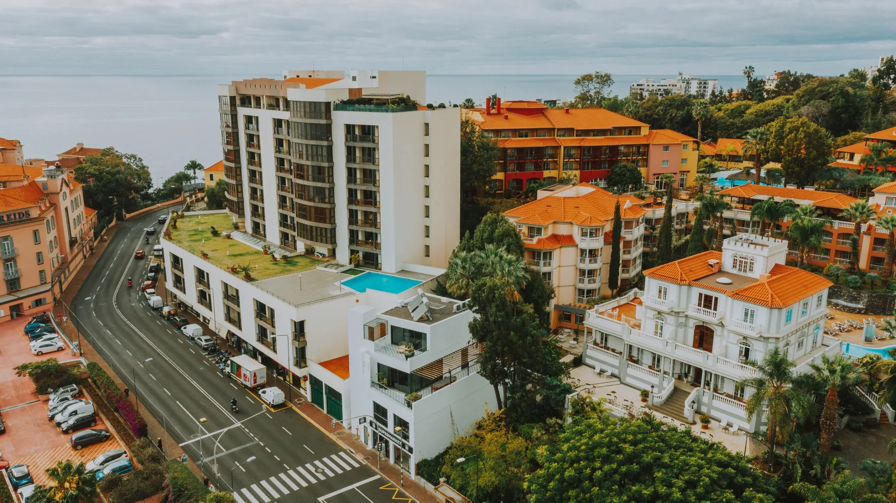 Una vista urbana con un edificio moderno, tejados de tejas rojas y una carretera curva.