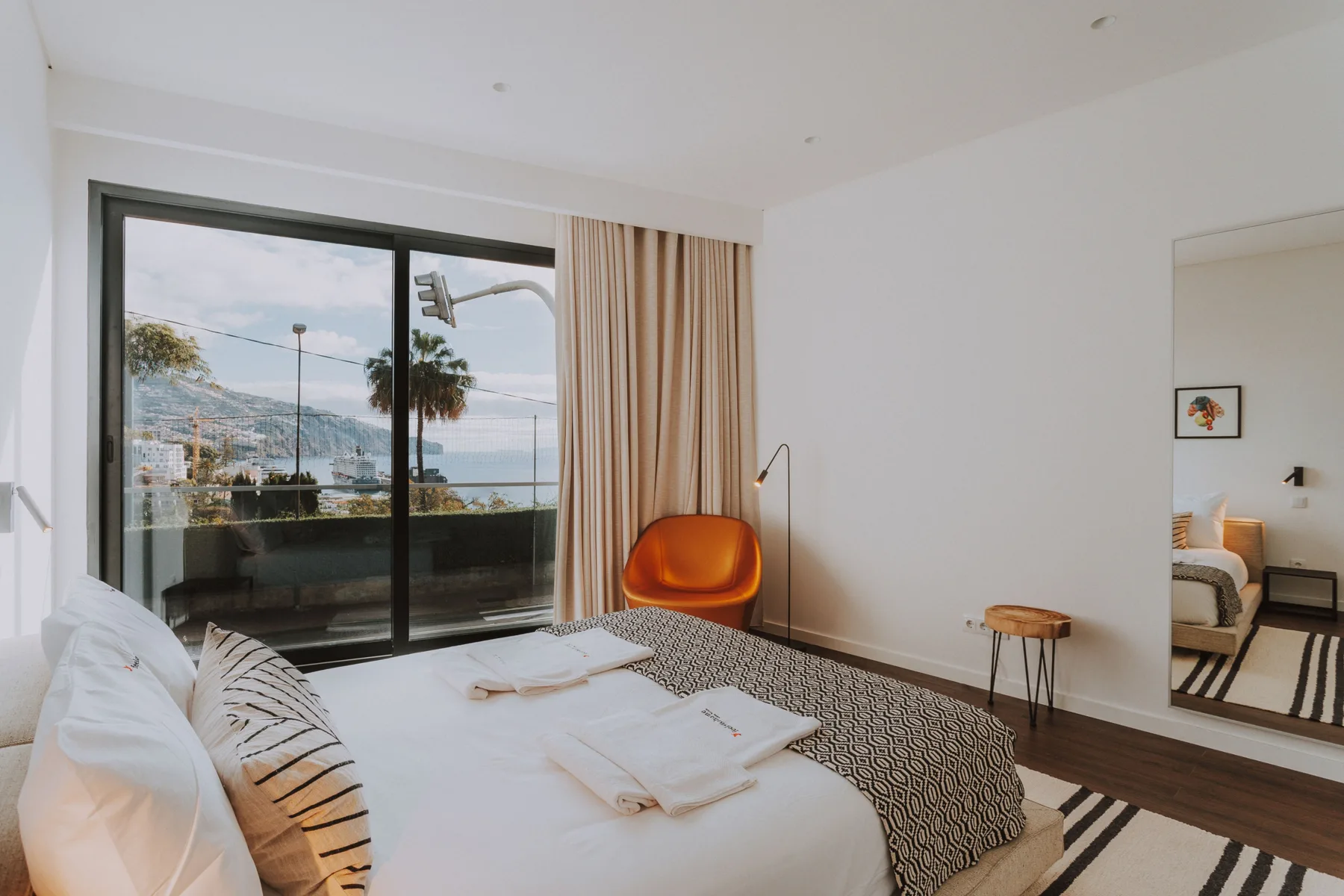 Un dormitorio luminoso con una cama grande y puertas corredizas de vidrio con vistas a la ciudad.