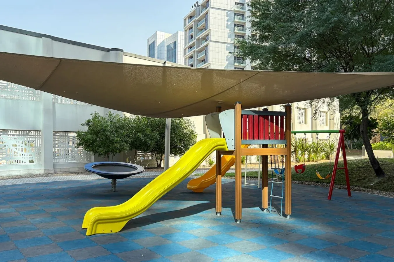 Un parque infantil al aire libre tiene un tobogán colorido, una estructura de juego y columpios.
