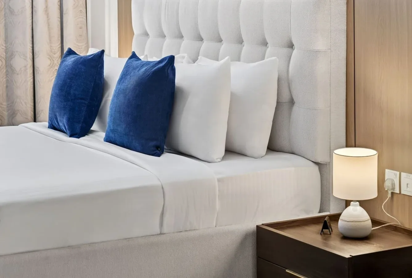Una cama bien tendida con almohadas azules y blancas está junto a una lámpara encendida.