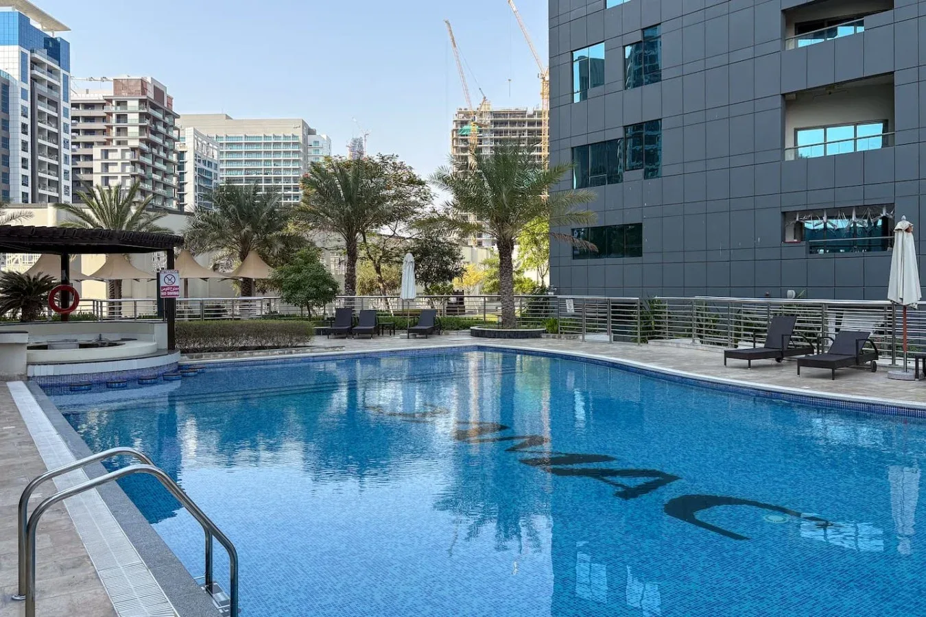 Una piscina al aire libre junto a un edificio moderno, con asientos de descanso en el borde.