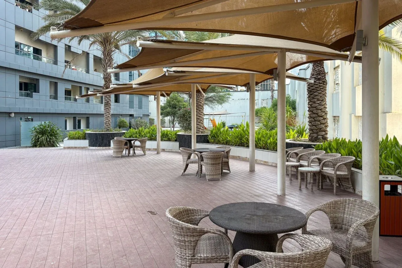 Un patio al aire libre con mesas redondas y asientos tejidos bajo toldos.