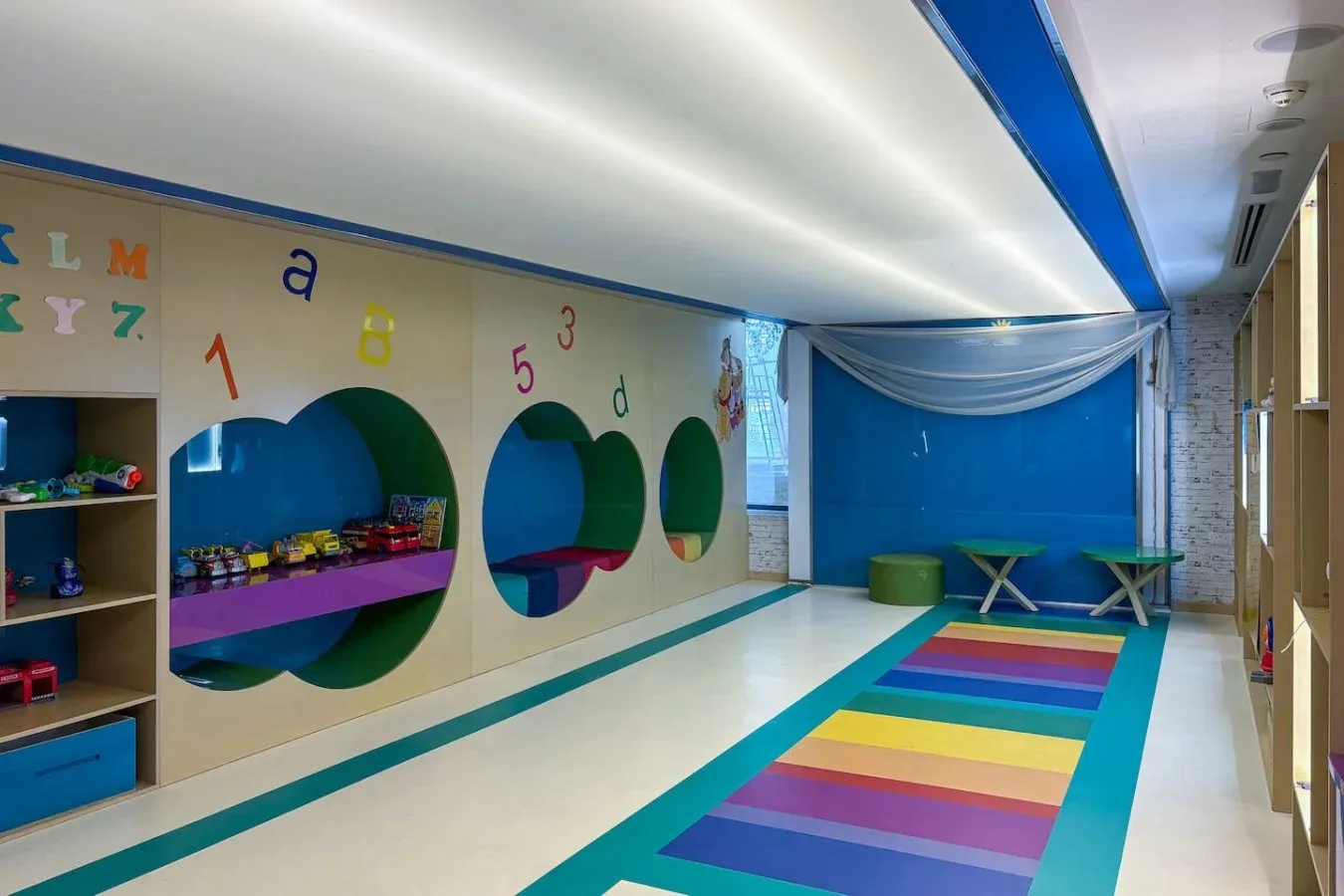 Una colorida sala de juegos infantil tiene una pared azul y un camino de franjas de colores.