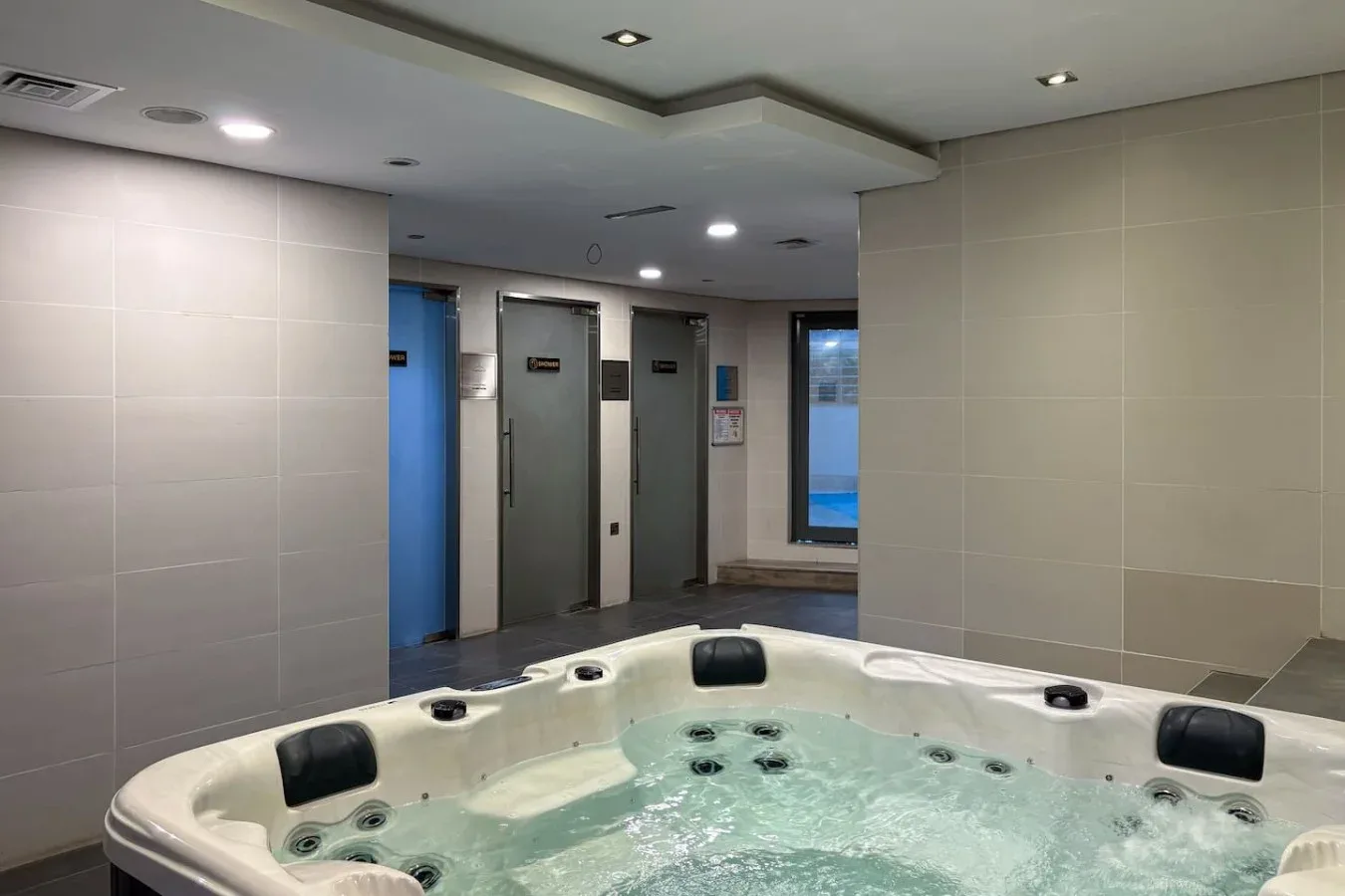 Una bañera de hidromasaje interior ocupa el primer plano de una sala revestida de azulejos.