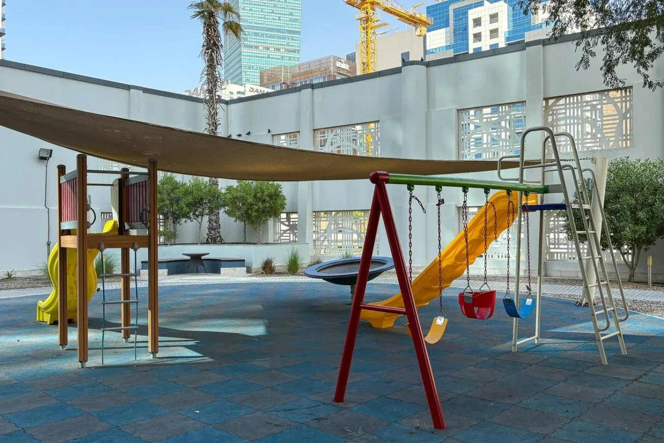 Un parque infantil al aire libre con columpios y toboganes bajo una cubierta de sombra.