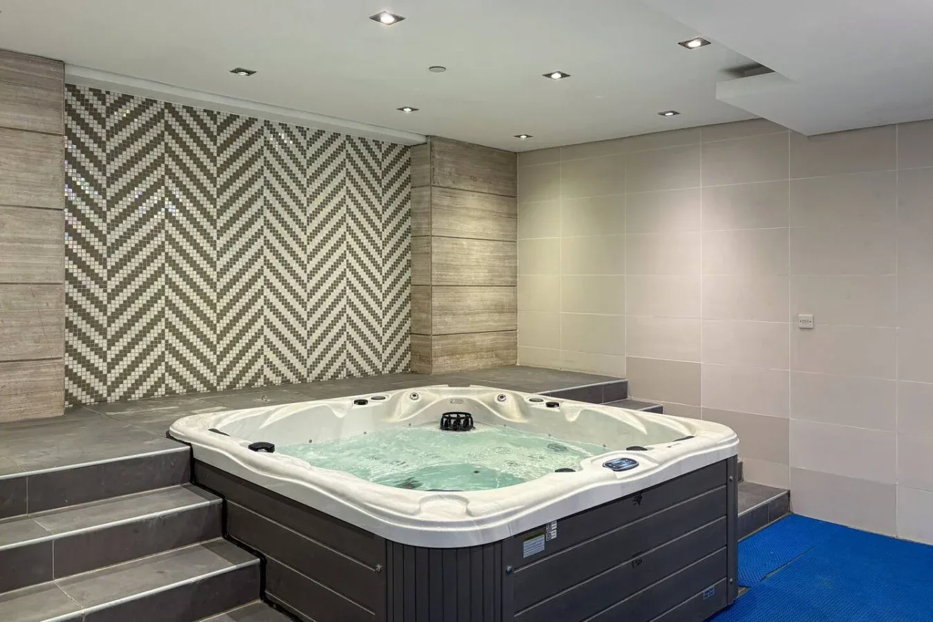 Una bañera de hidromasaje interior está junto a paredes de azulejos y una pared decorativa estampada.