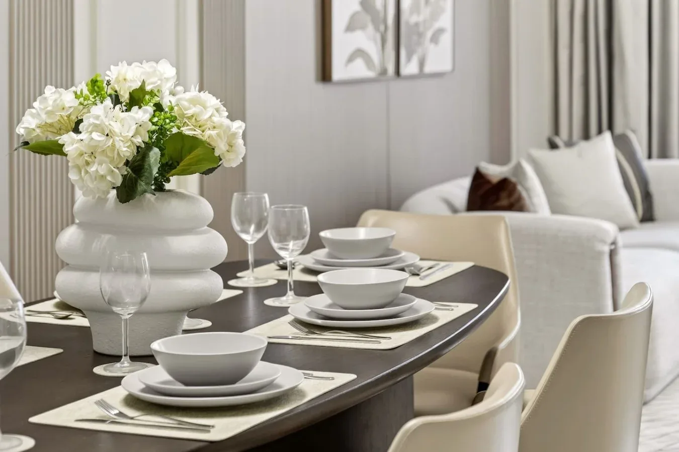 Una mesa de comedor preparada con vajilla blanca y flores, junto a una sala de estar.