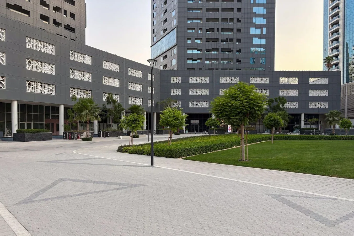 Un patio pavimentado con césped y árboles frente a edificios modernos de gran altura.