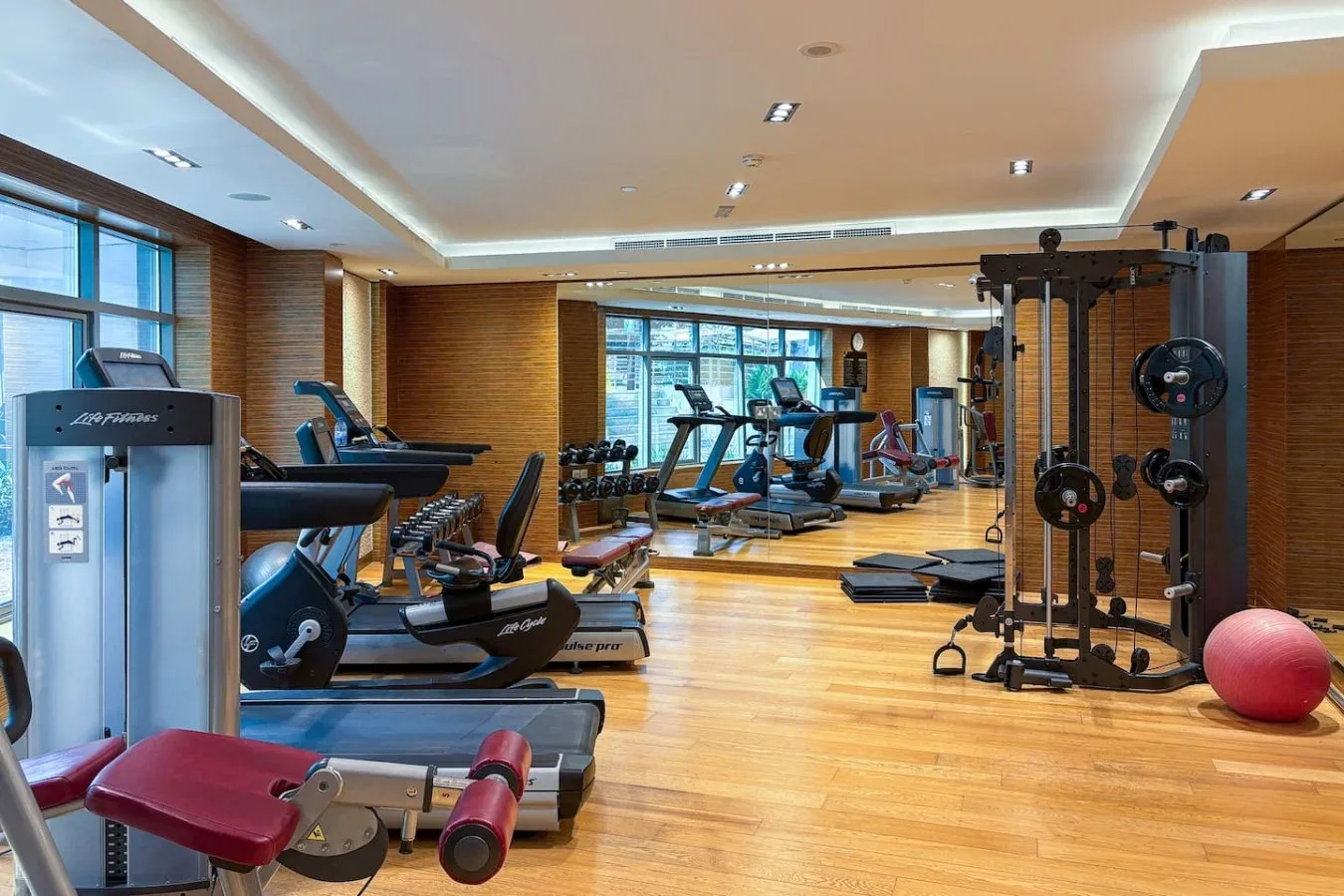 Un gimnasio con máquinas de ejercicio, pesas y una pelota roja.