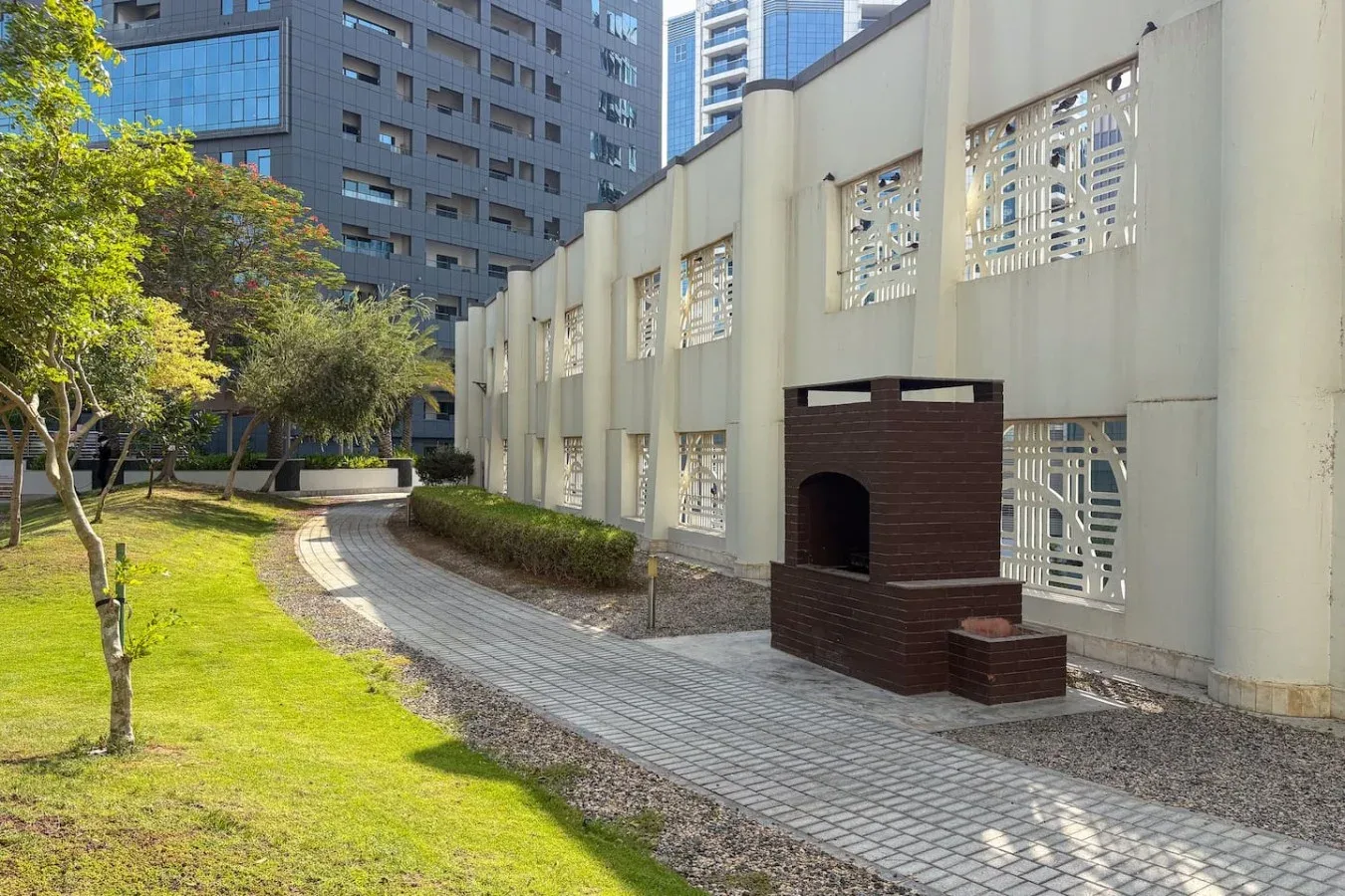 Un camino pavimentado curva junto a un patio con césped y un edificio claro.
