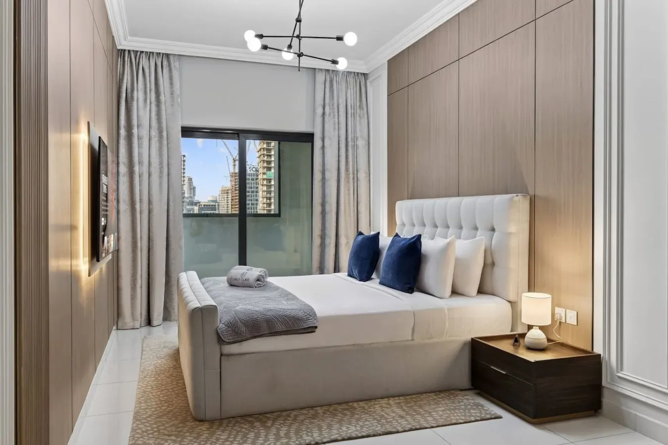 Un dormitorio con una cama tendida junto a una ventana con edificios a la vista.