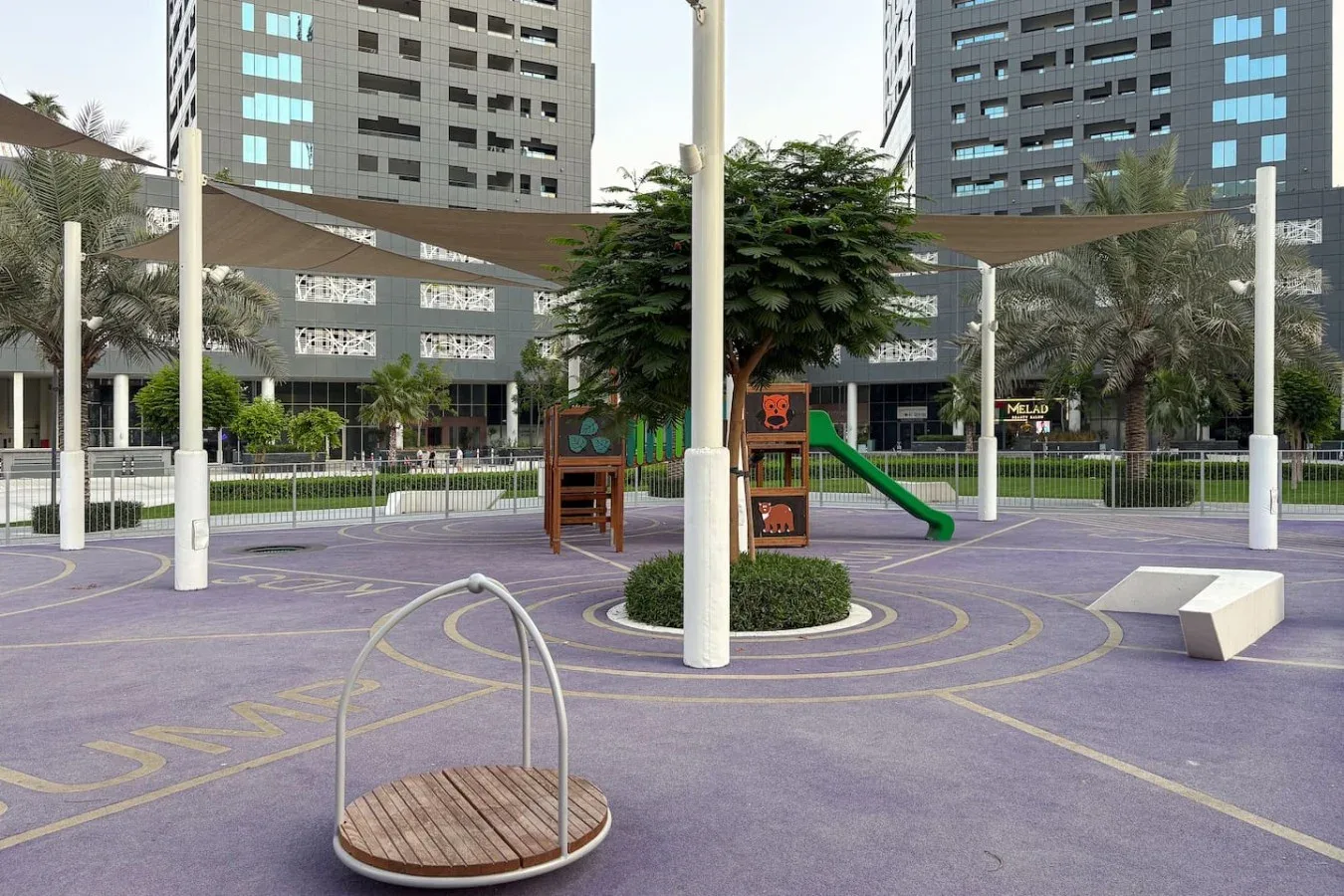 Un parque infantil al aire libre con juegos de colores y un árbol frondoso.
