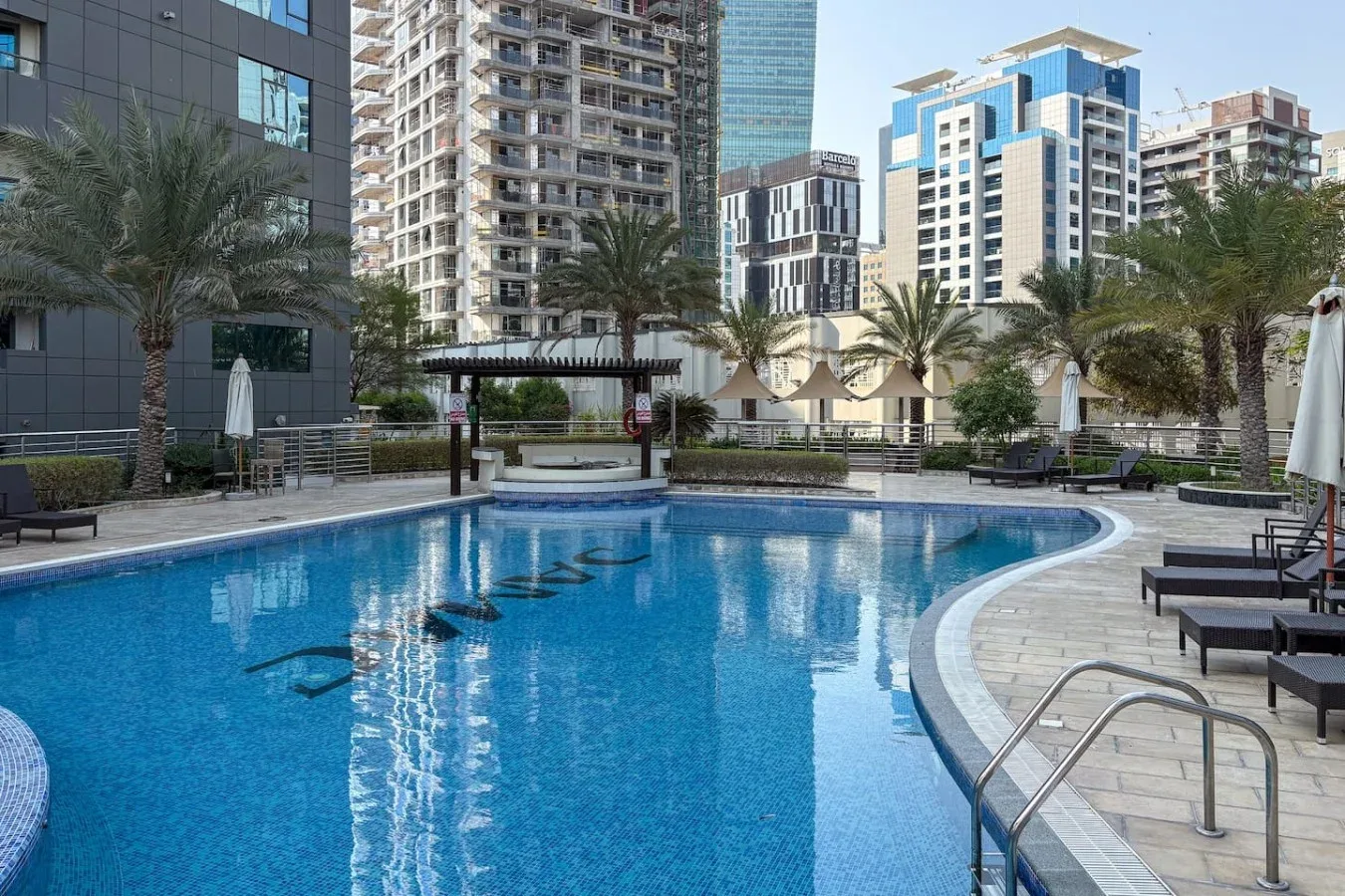 Una piscina con asientos de descanso y palmeras entre los edificios circundantes.