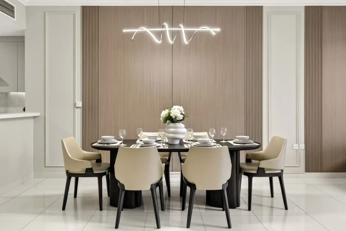 Un comedor con la mesa puesta y un arreglo floral bajo una lámpara moderna.