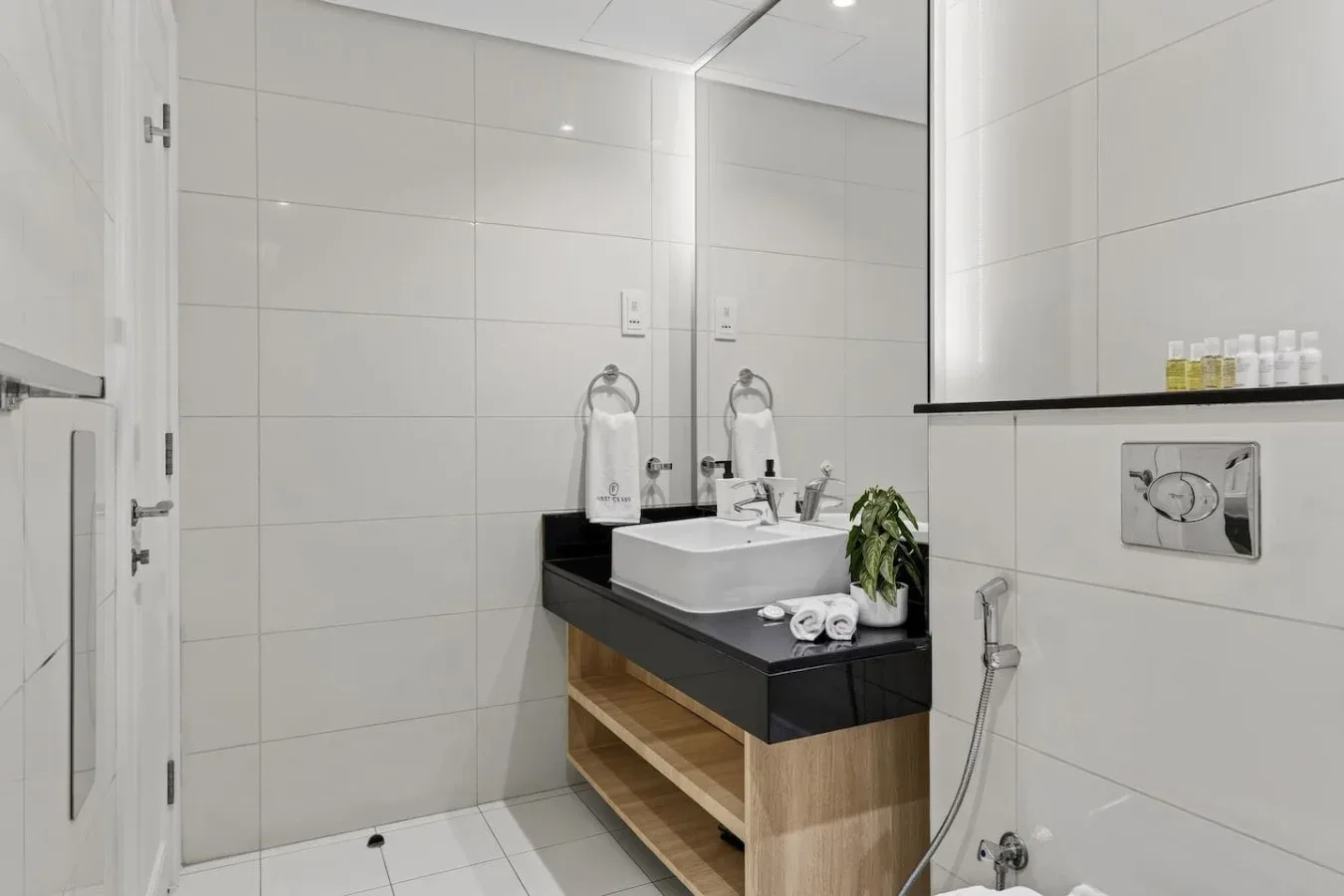 Un baño alicatado con lavabo, espejo y controles de ducha en la pared.