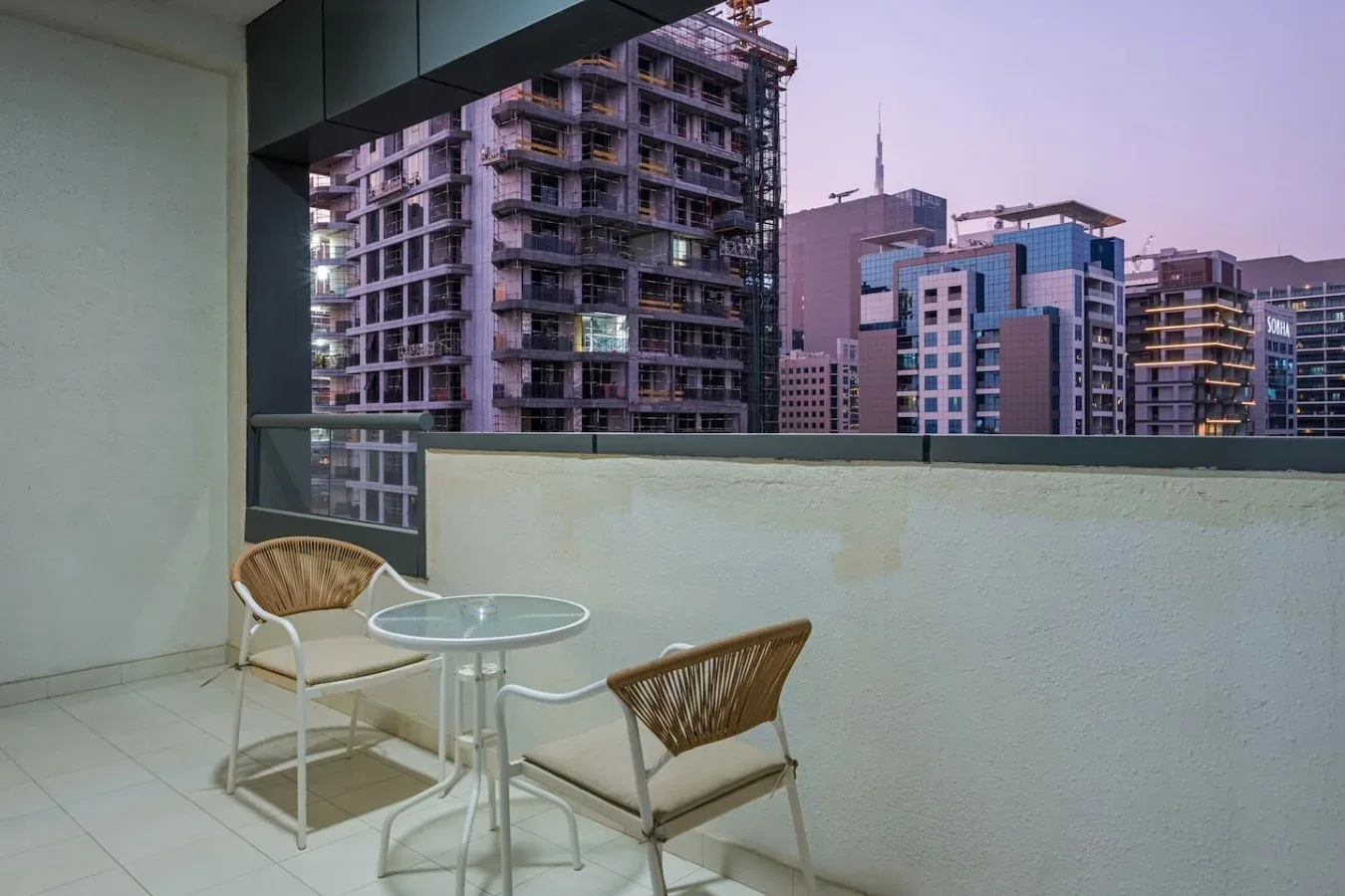 Una zona de descanso en el balcón con una mesa redonda mira hacia edificios cercanos.