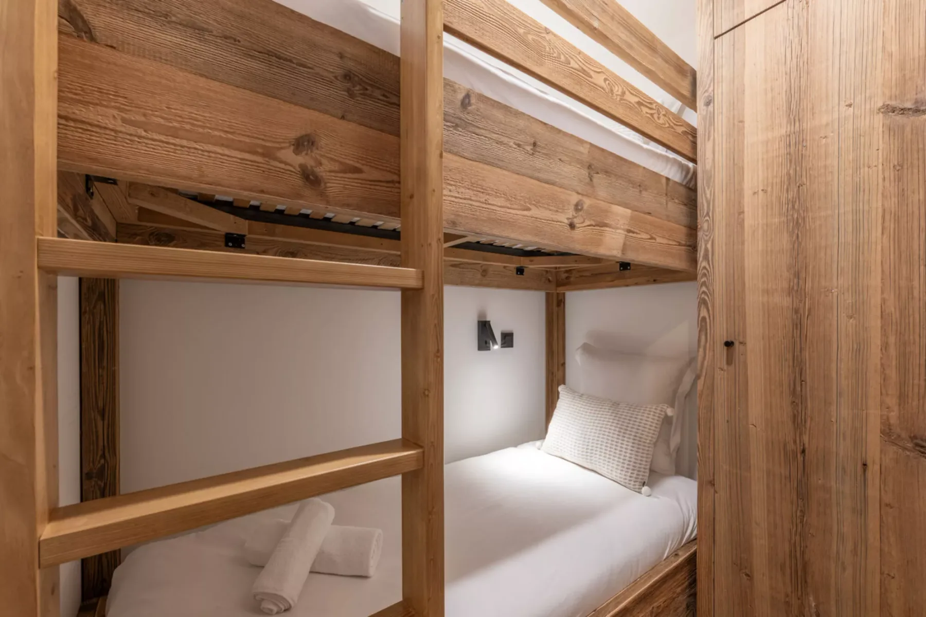 A compact bunk-bed sleeping area with white bedding and a wooden ladder.