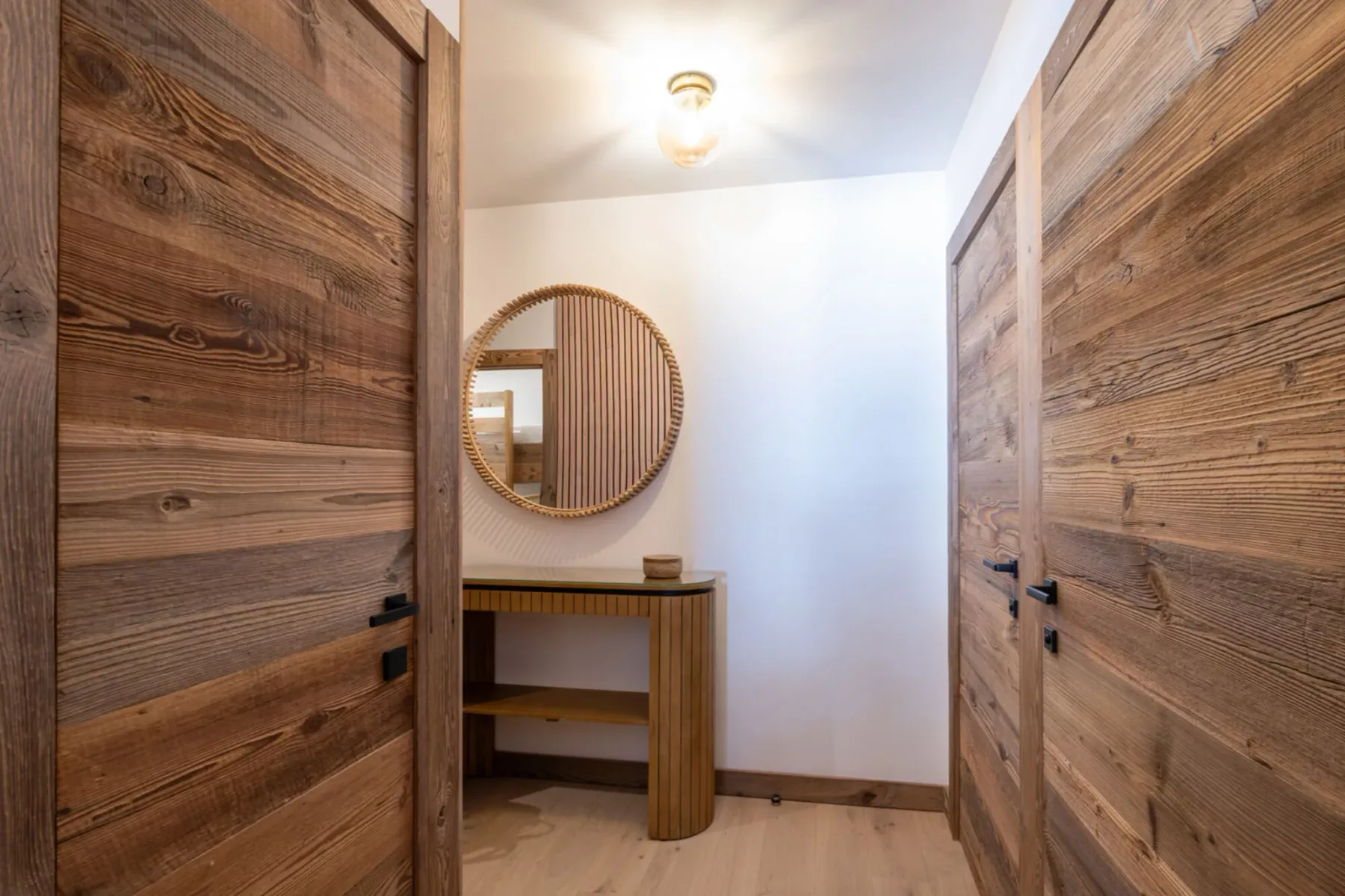 A wooden hallway with paneled doors and a round mirror above a console table.