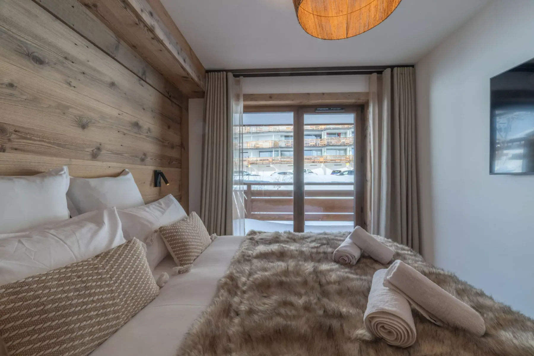 A bedroom with a bed, textured bedding, and glass doors opening onto a balcony.