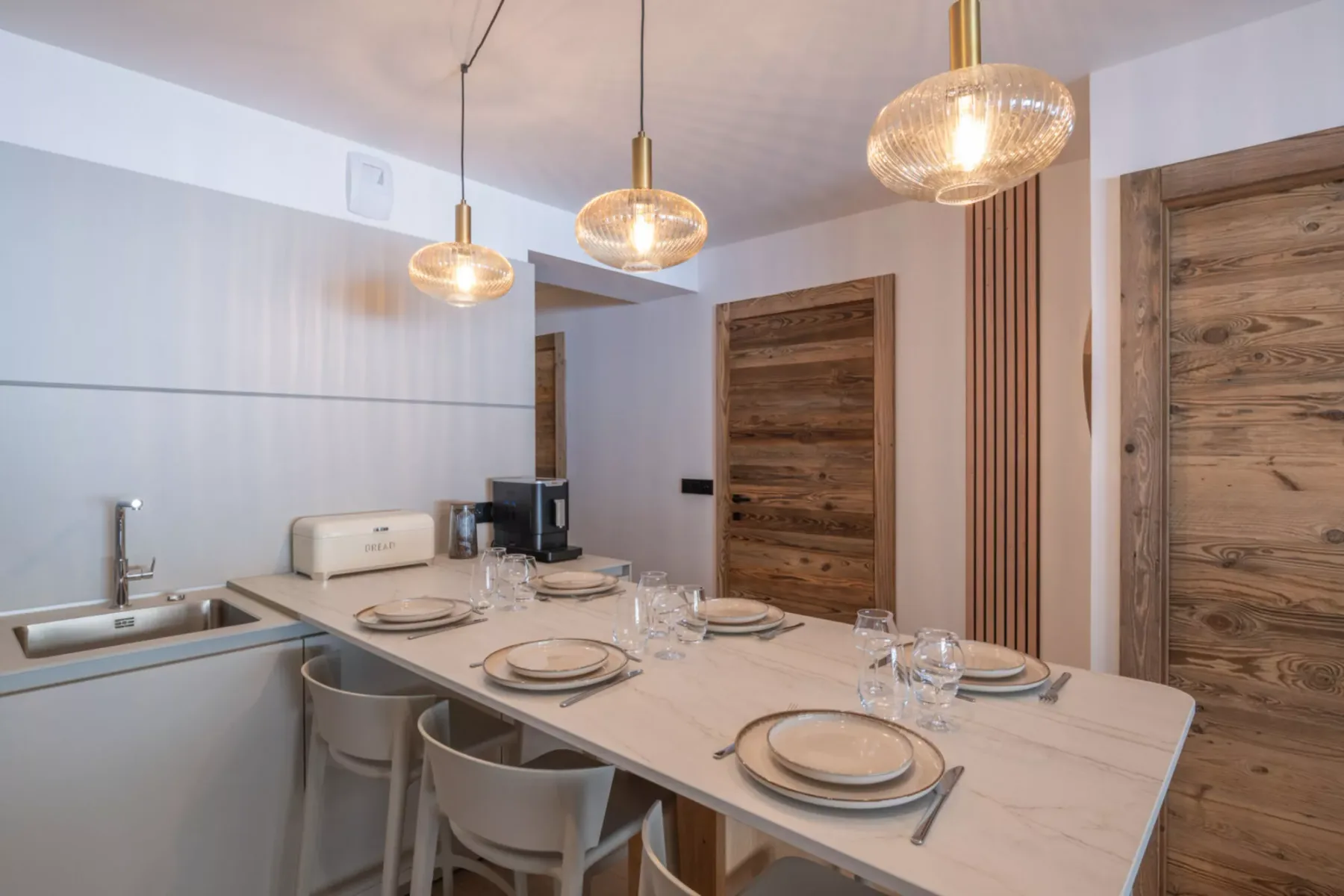 A dining area with a long table set with plates beneath pendant lights.
