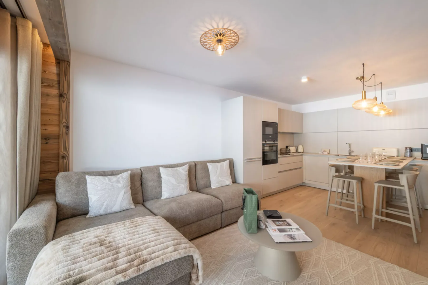 A modern living room opens into a kitchen, with a sectional and dining island.