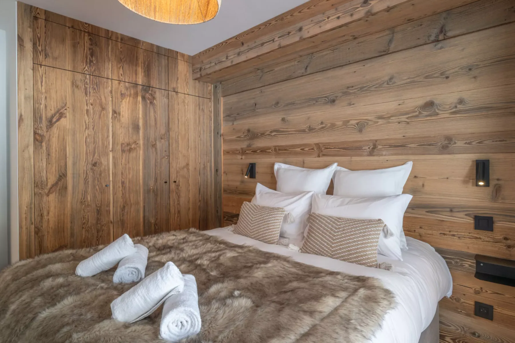 A bedroom with a bed against a wood-paneled wall.